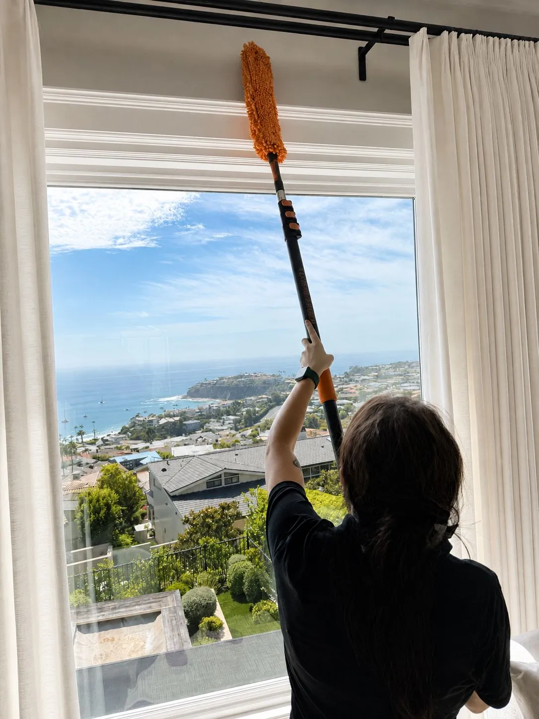 Gabby dusting tall window trim in a Laguna Beach hillside home overlooking the Pacific