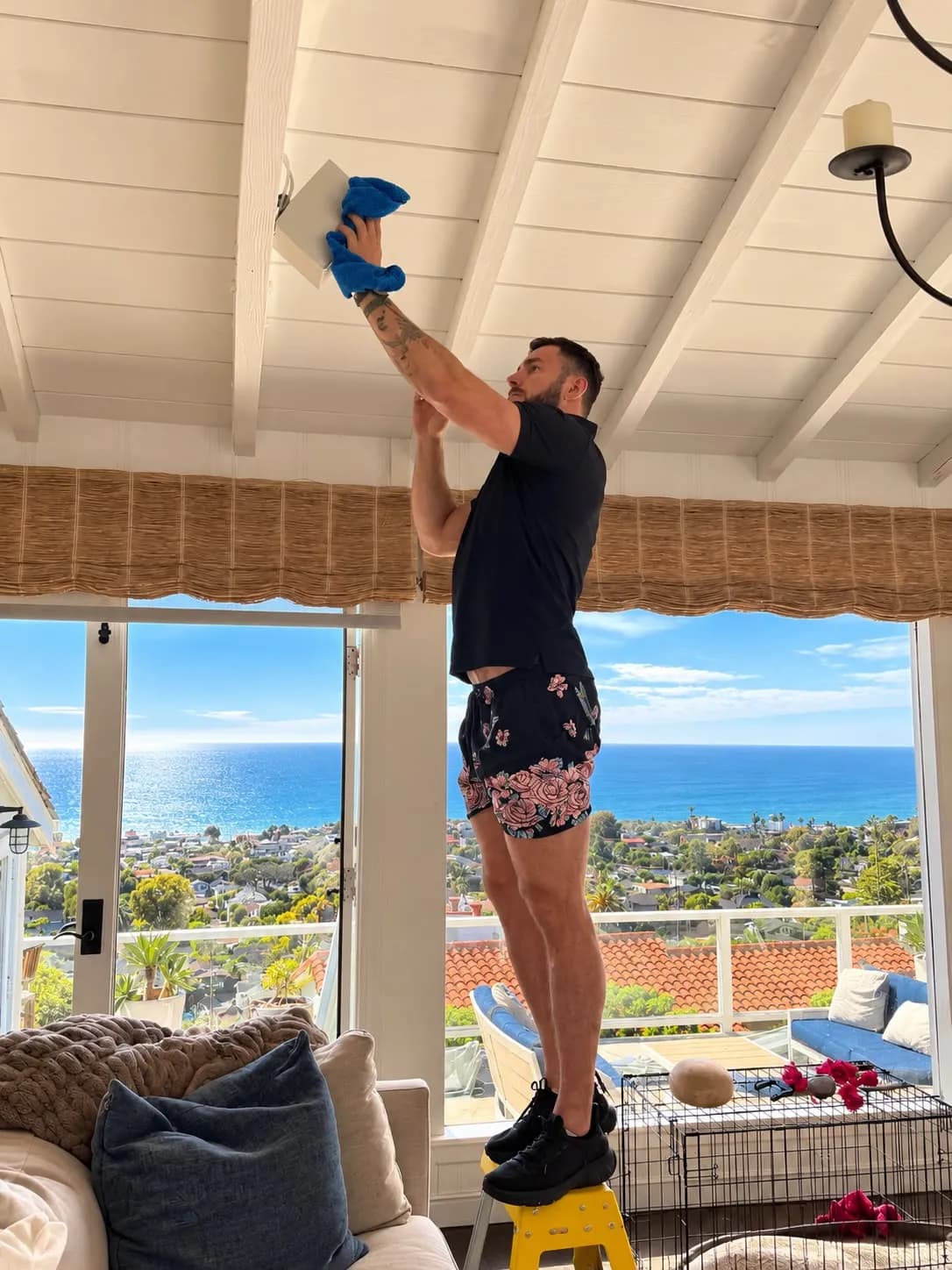 Dusting a ceiling light on a beamed ceiling in an ocean-view living room